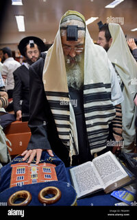 An orthodox jewish man reads from a prayer book with his hand on a F8GA4H