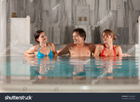 Stock photo three friends one man and two women in swimming pool or thermal bath doing wellnes Stock photo three friends one man and two women in swimming pool or thermal bath doing wellnes