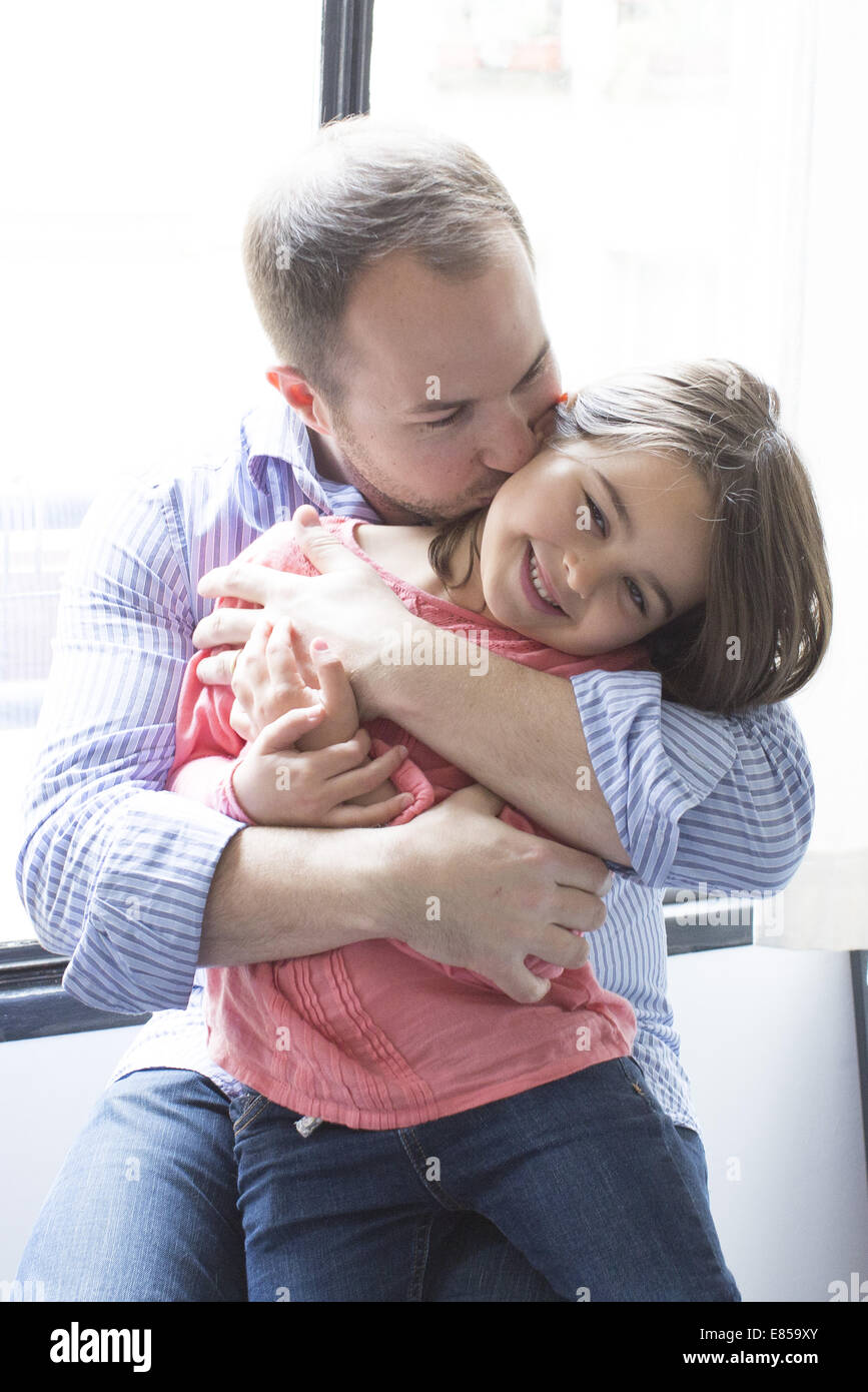 father-holding-daughter-on-his-lap-kissing-her-cheek-E859XY.jpg