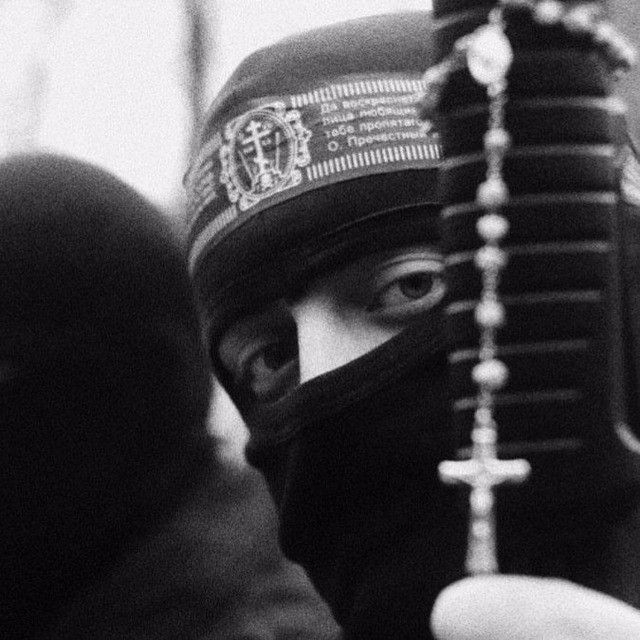 This may contain: a person wearing a black mask and holding up a small object to their face while standing next to another person