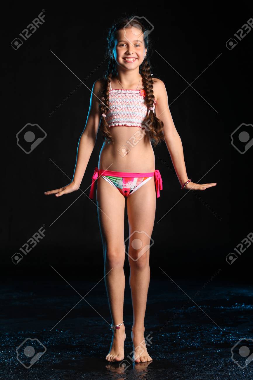 93310790-happy-young-teenage-girl-in-a-swimsuit-stands-barefoot-on-a-black-background-pretty-child-with-dark-.jpg