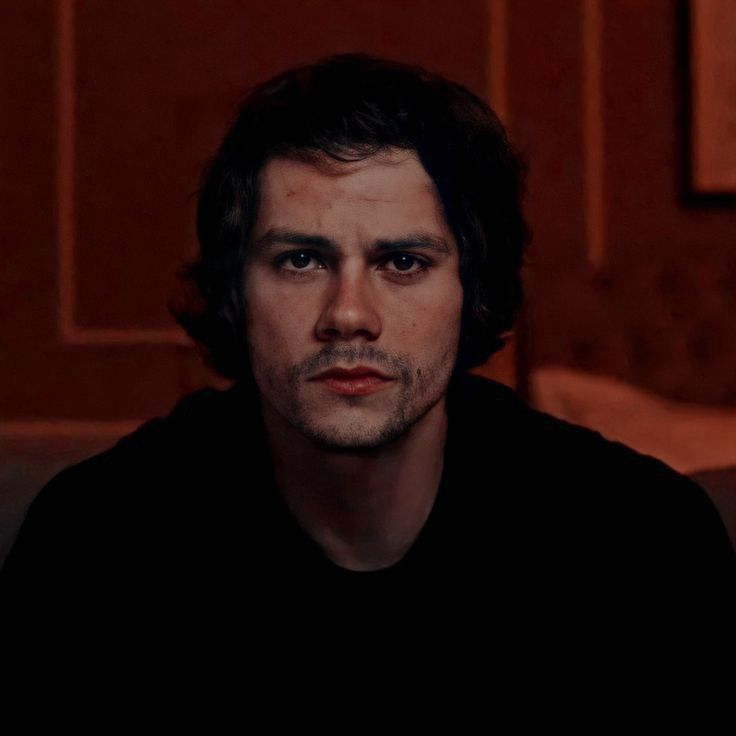 This may contain: a man with long hair sitting on a couch looking at the camera while wearing a black shirt