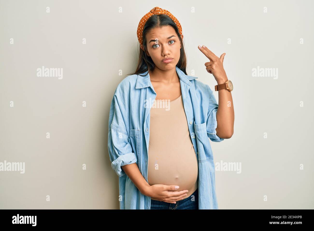 beautiful-hispanic-woman-expecting-a-baby-touching-pregnant-belly-shooting-and-killing-oneself-pointing-hand-and-fingers-to-head-like-gun-suicide-ge-2E34XPB.jpg