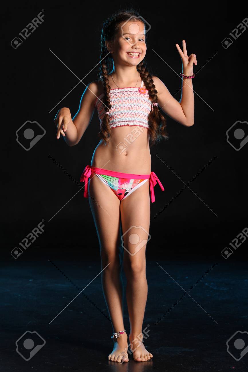 93364155-happy-young-teenage-girl-in-a-swimsuit-stands-barefoot-on-a-black-background-pretty-child-with-dark-.jpg