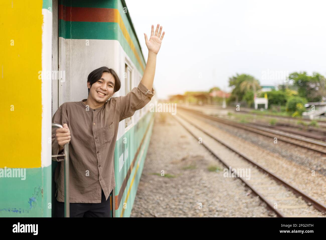 handsome-young-asian-man-hand-to-say-hello-or-goodbye-to-friend-on-train-waving-goodbye-2FG2XTH.jpg