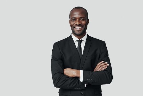 Photo handsome young african man in formalwear looking at camera and smiling while standing against grey wall