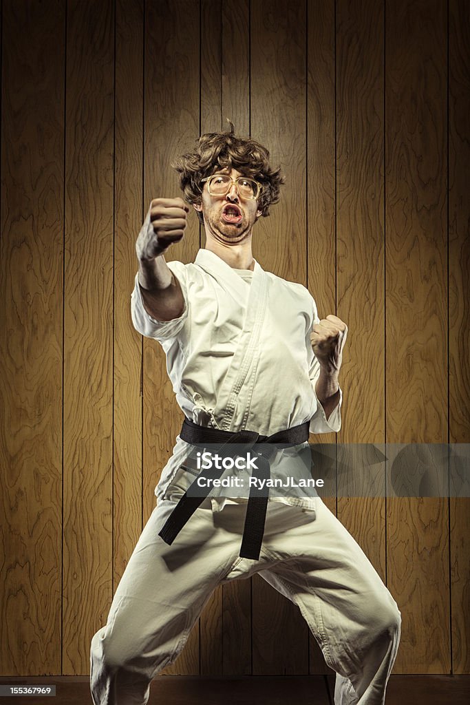 Black Belt Karate Nerd Man A nerdy looking kung fu master guy wearing a white gi and a black belt stands in a horse stance and punches into the air at his dojo as he practices martial arts.  He makes a goofy face behind his giant glasses in front of a wood paneled wall.  Vertical with copy space. Karate Stock Photo