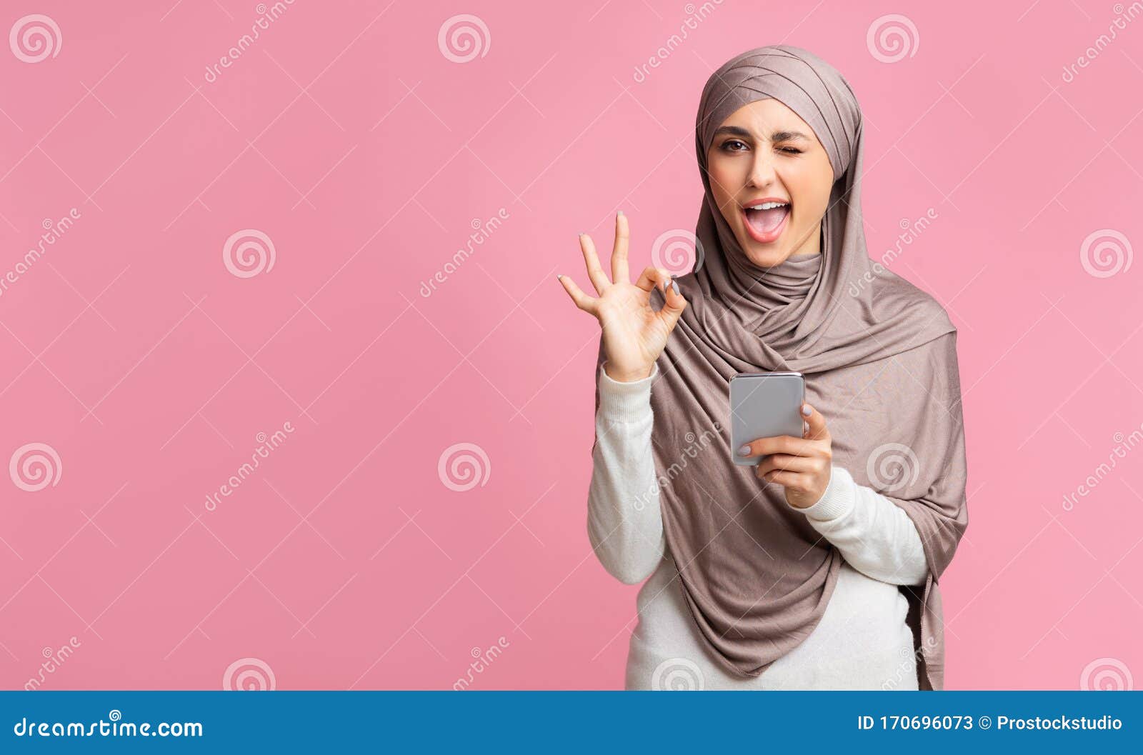 arabic-woman-hijab-using-smartphone-winking-showing-ok-gesture-cool-islamic-app-positive-muslim-girl-hijab-winking-170696073.jpg