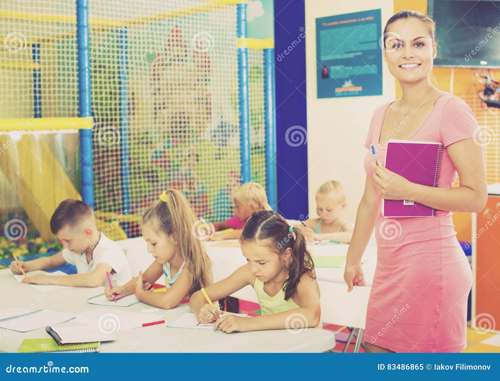 young-smiling-woman-teacher-standing-textbook-women-school-class-kids-83486865.jpg
